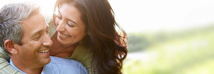 Close-up of two adults outdoors, leaning together with blurred green background and soft natural lighting.