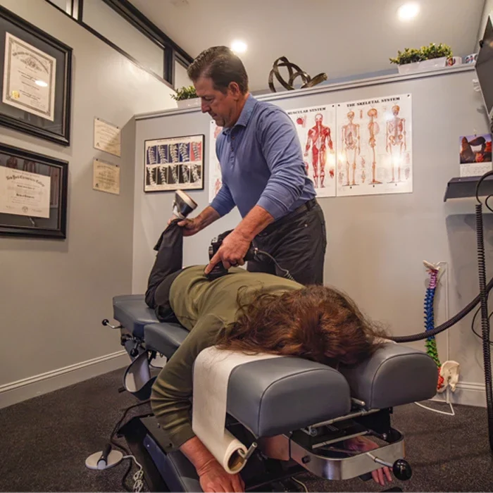 Dr. Richard Kuhns using a handheld device on a person lying face down on a padded table in a room with anatomy charts.